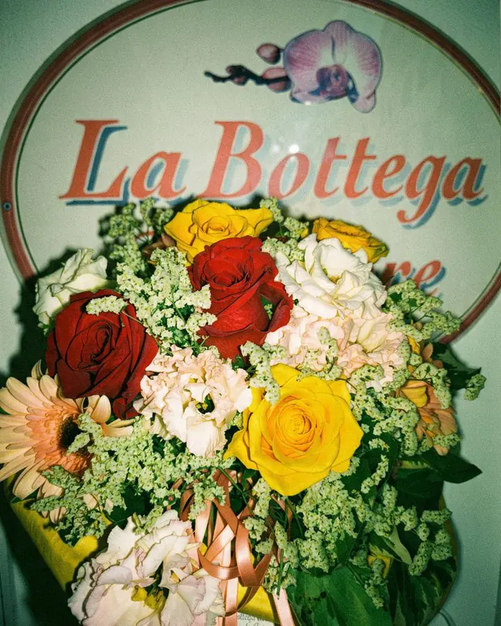 Bouquet di rose, gerbere e lisianthus davanti all’insegna La Bottega
