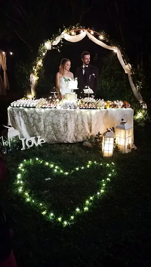 Buffet di dolci sotto un arco con tulle, luci e lanterne per i festeggiamenti di un matrimonio