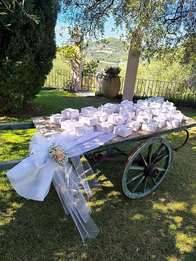 Carretto d’epoca nel giardino con scatoline bonbonniere bianche e fiocco di tulle con rosa