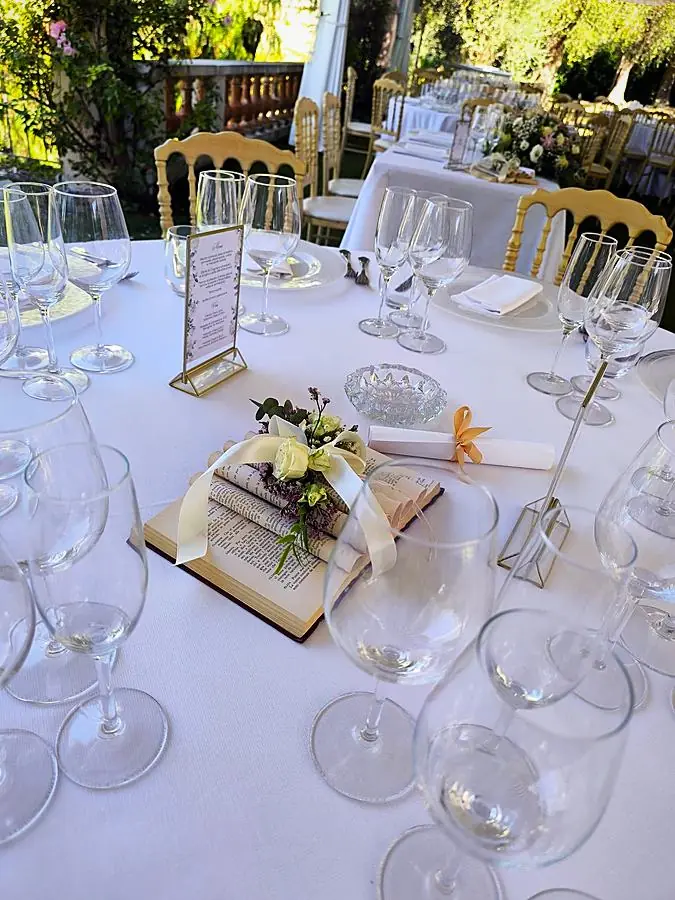 Centrotavola con libro aperto, fiori e pergamena su un tavolo di ricevimento in giardino