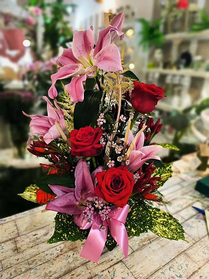 Composizione di gigli rosa, rose rosse e peperoncini decorativi con fiocco rosa