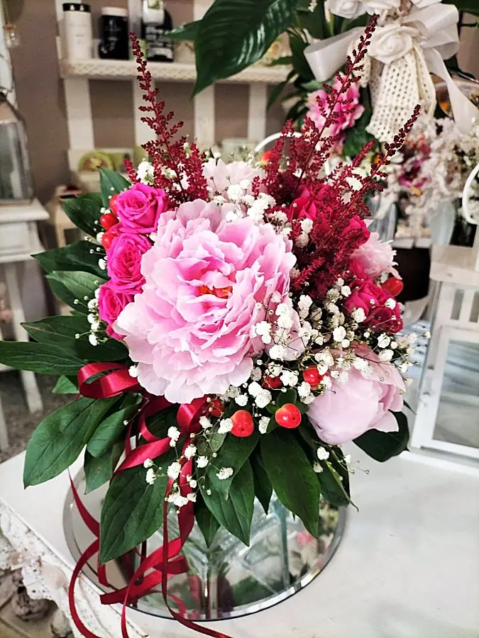 Composizione di peonie rosa, rose fucsia e bacche rosse con nastro bordeaux