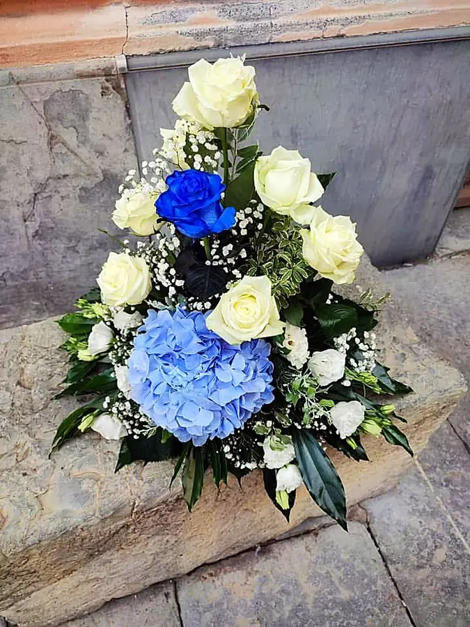 Composizione di rose bianche, ortensia azzurra e una rosa blu su pietra
