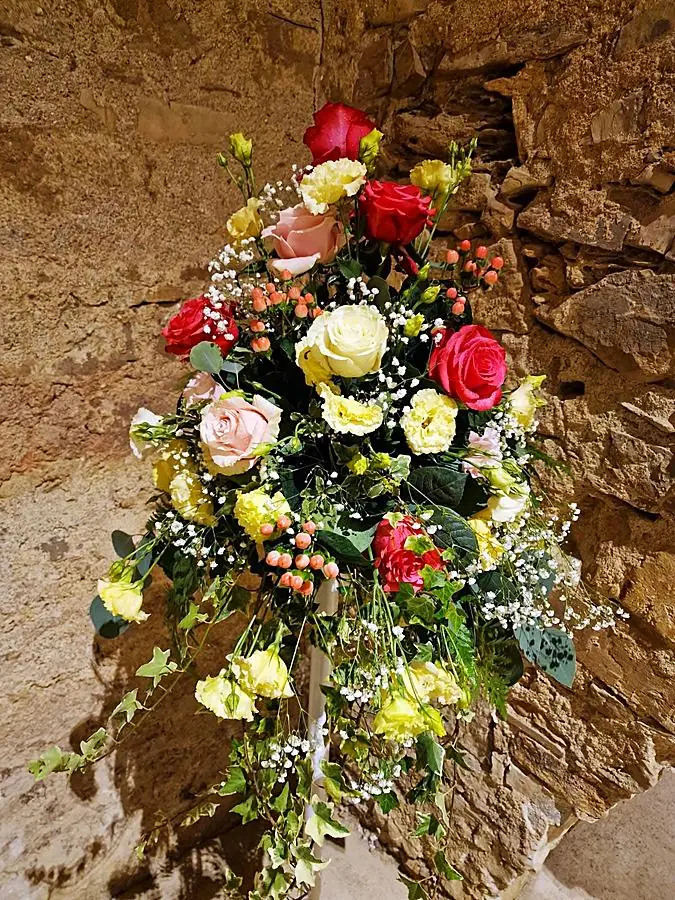 Composizione di rose, lisianthus gialli e bacche davanti a una parete di pietra