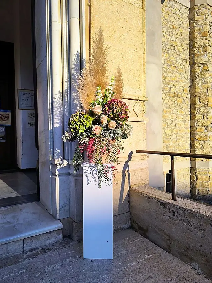 Composizione di rose, ortensie, pampas e pepe rosa su colonna bianca all’ingresso di una chiesa