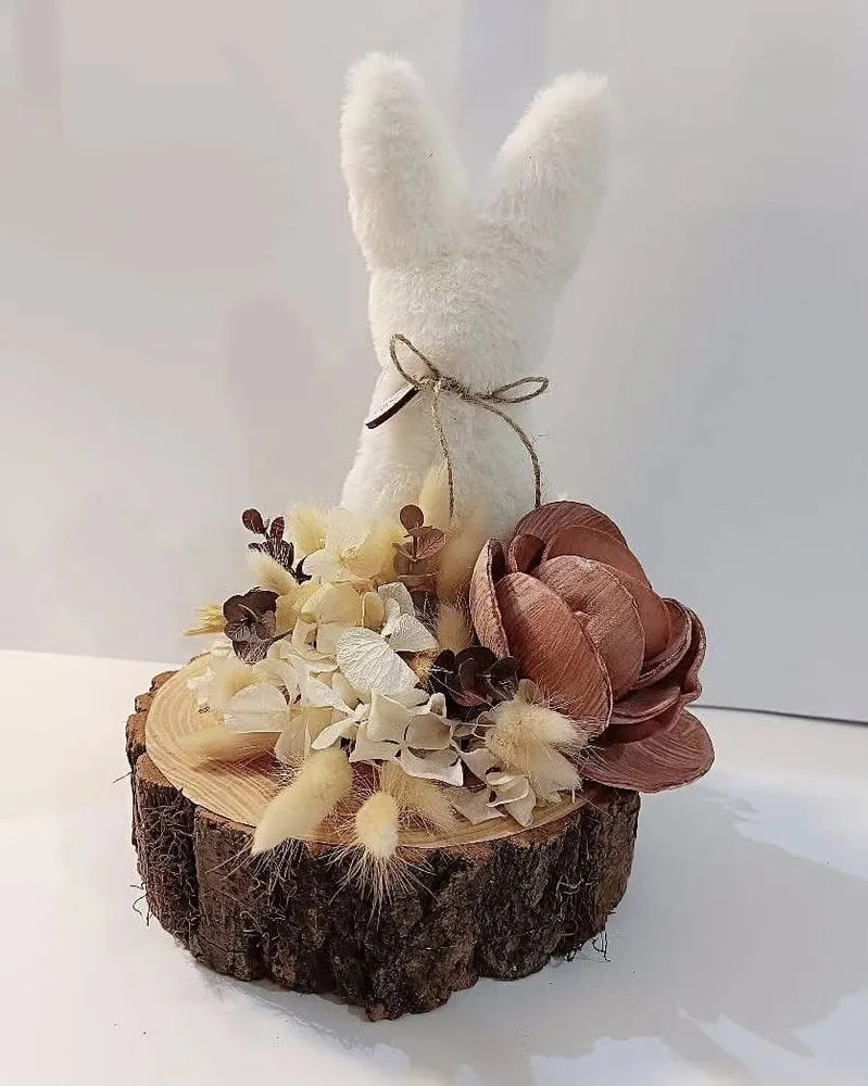 Coniglietto di peluche su tronchetto di legno con fiori secchi, ortensie bianche e fiore di legno rosato