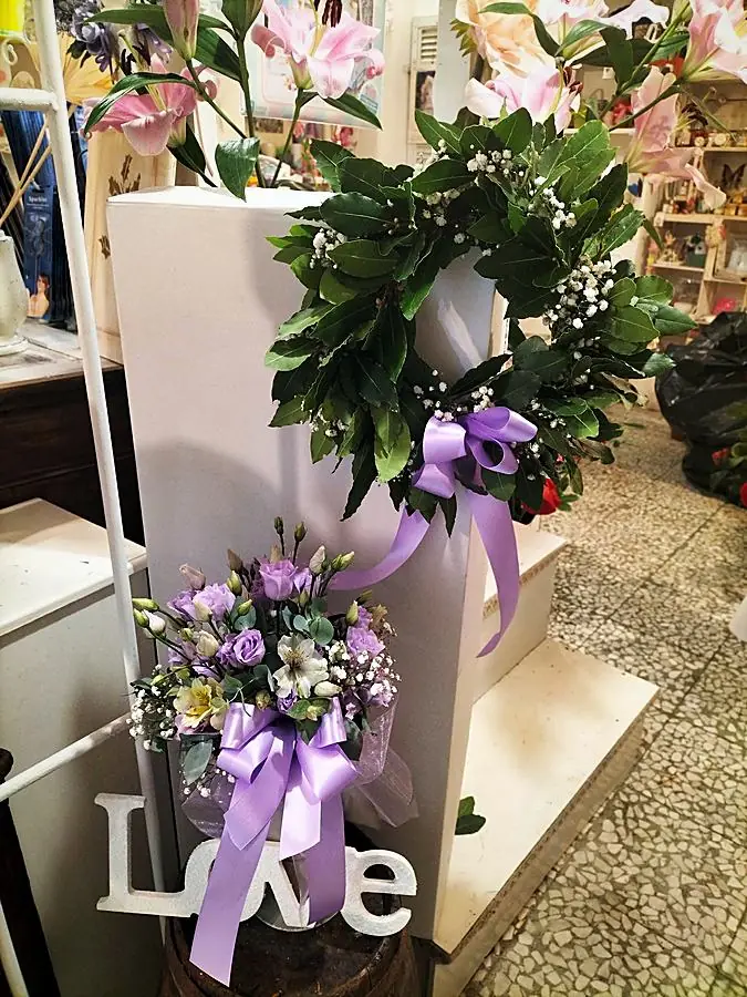 Corona d’alloro con nastro lilla e bouquet di lisianthus lilla accanto alla scritta Love