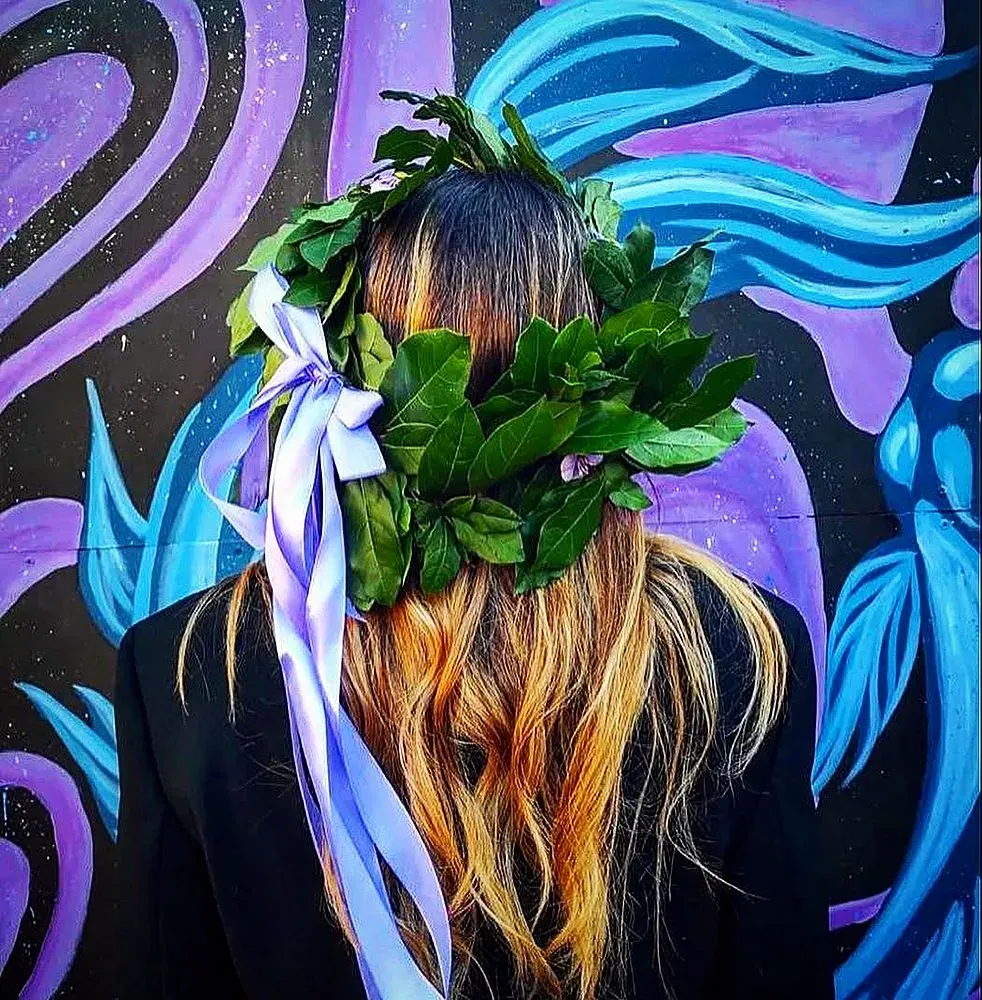 Corona d’alloro con nastro lilla per una laurea, davanti a un murale colorato