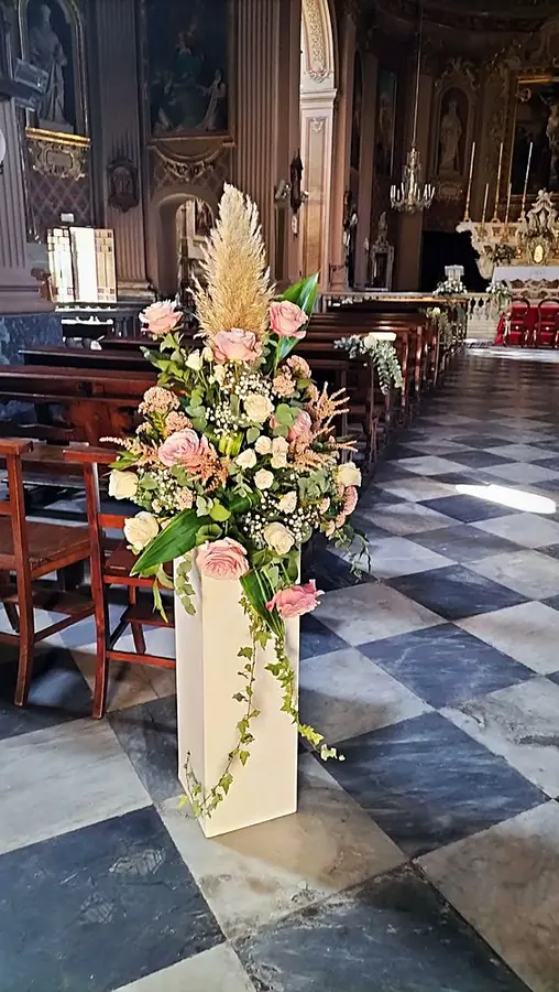 Grande composizione di rose rosa e bianche con erba delle pampas su colonna bianca in chiesa