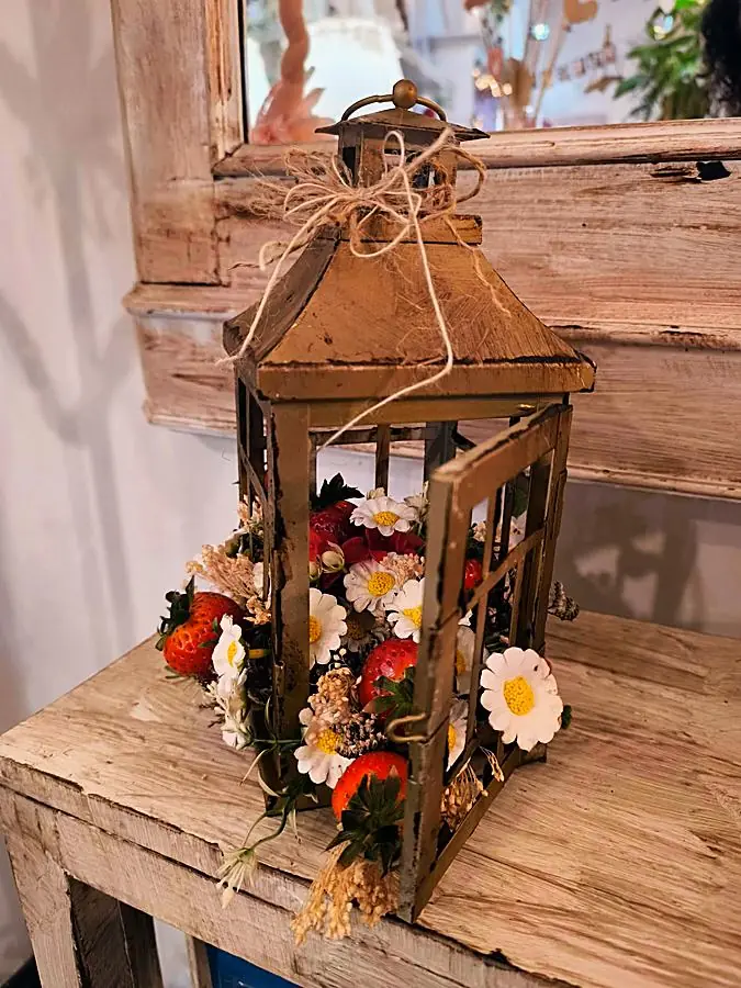 Lanterna d’epoca con margherite, fragole e fiori secchi, chiusa da un nodo di spago