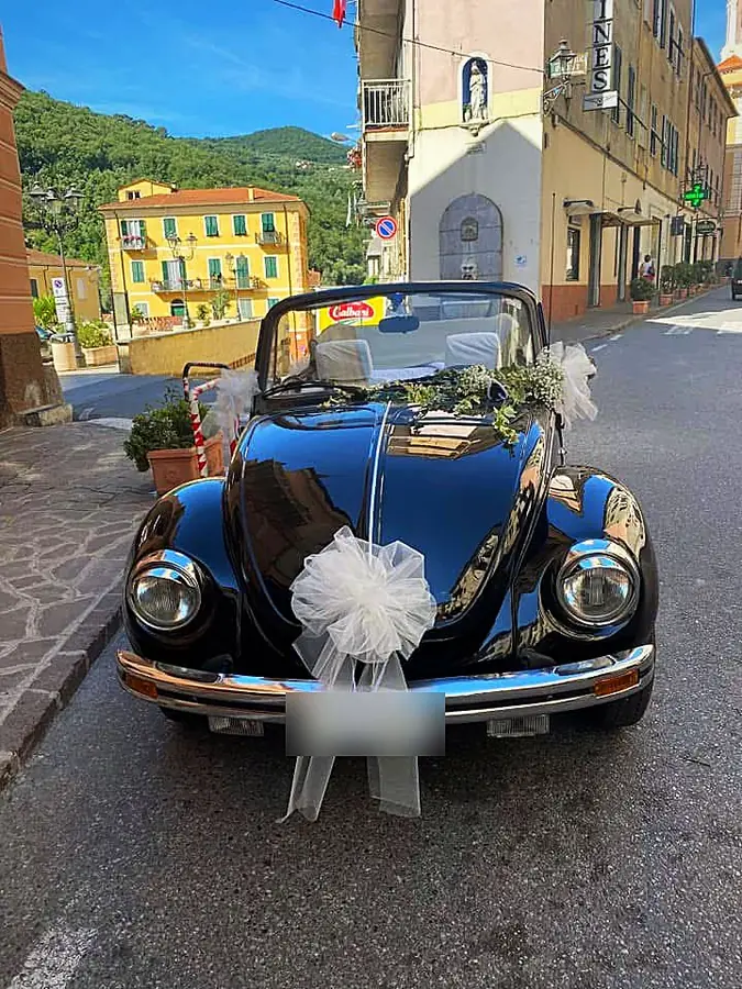 Maggiolino cabrio nero addobbato con grande fiocco bianco e rametti verdi per un matrimonio