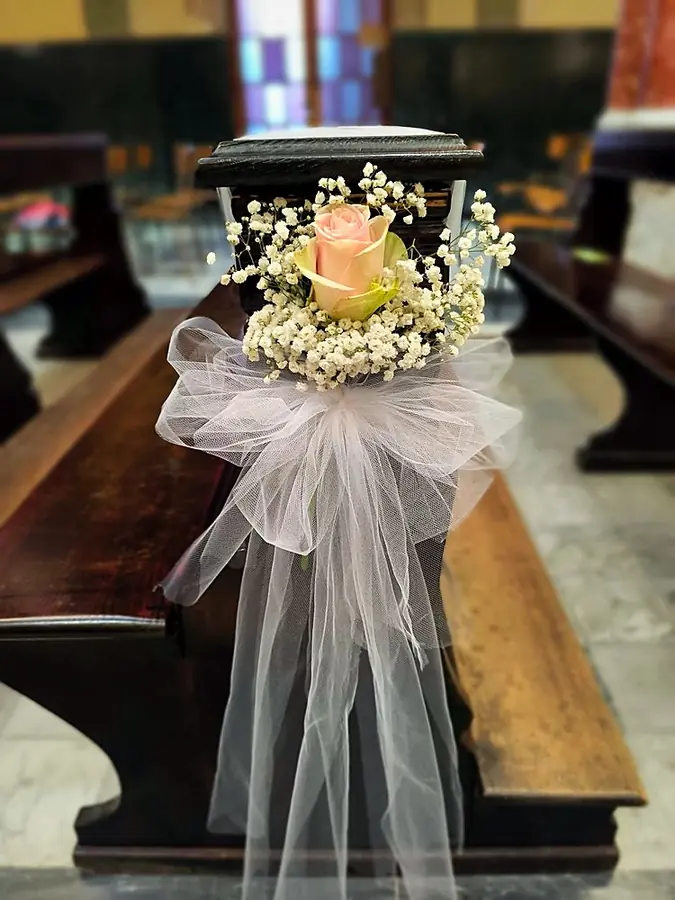 Rosa rosa con gypsophila e tulle bianco sul fine panca di una chiesa
