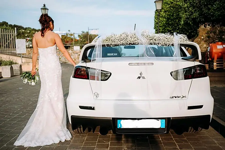 Sposa accanto all’auto bianca decorata con nuvole di gypsophila e tulle