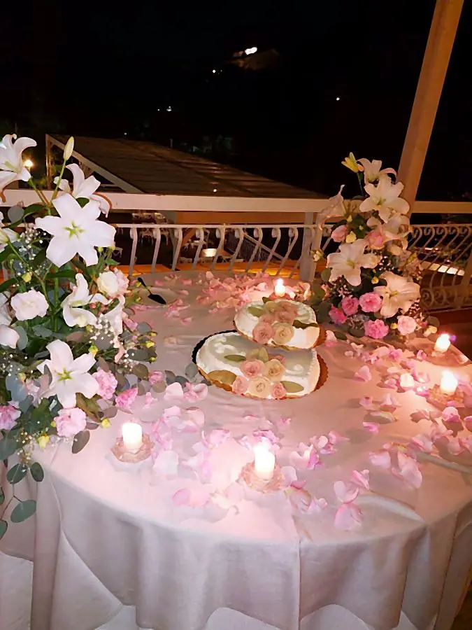 Torta nuziale con petali di rosa, candele e composizioni di gigli rosa e bianchi